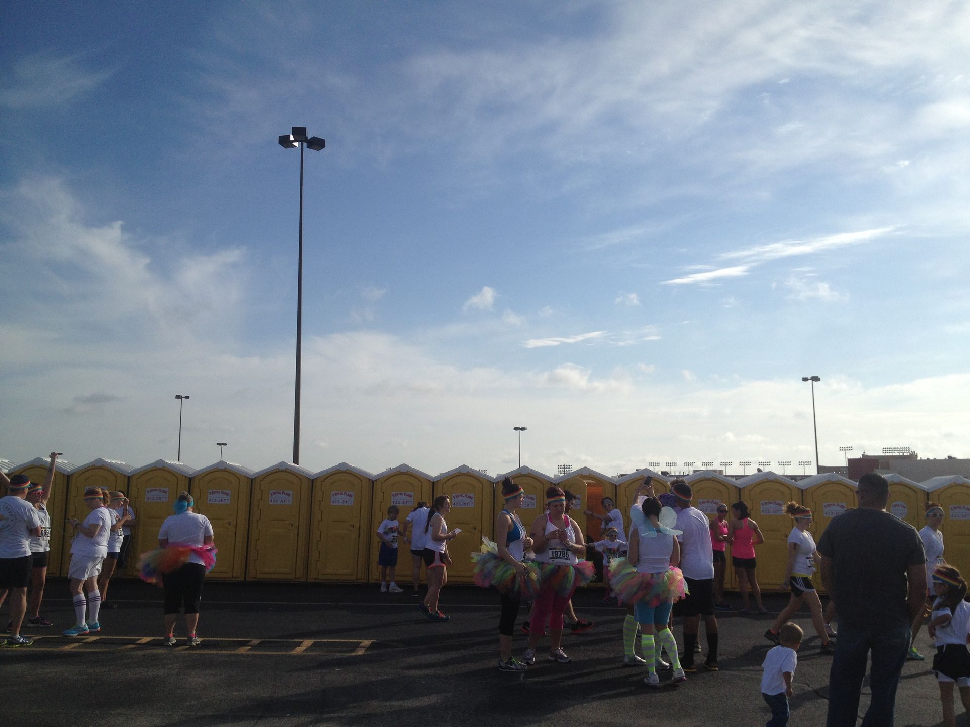 People gather by a row of yellow portable toilets under a cloudy blue sky.