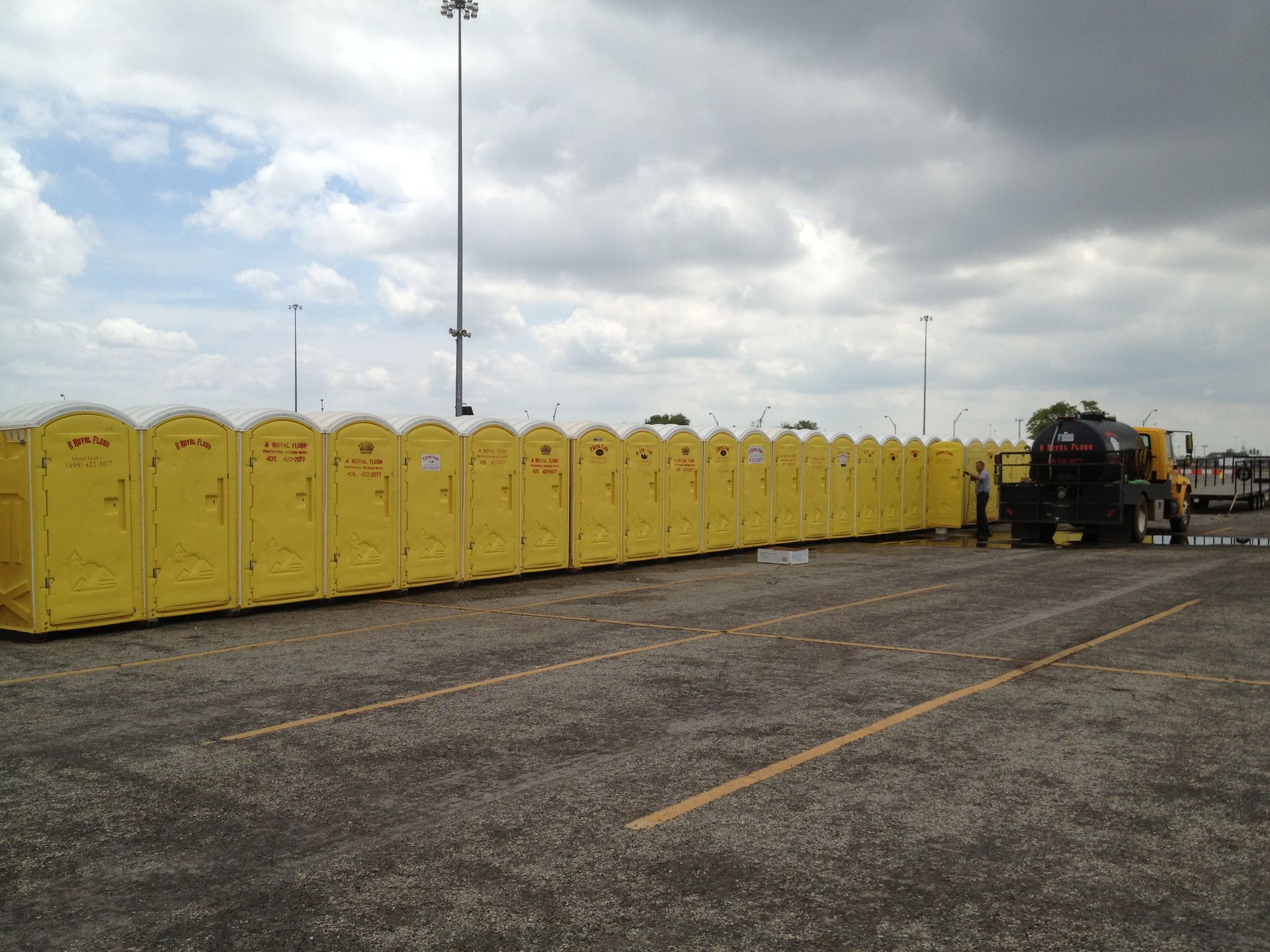 Yellow portable toilets lined up in a parking lot, a truck near them under a cloudy sky.