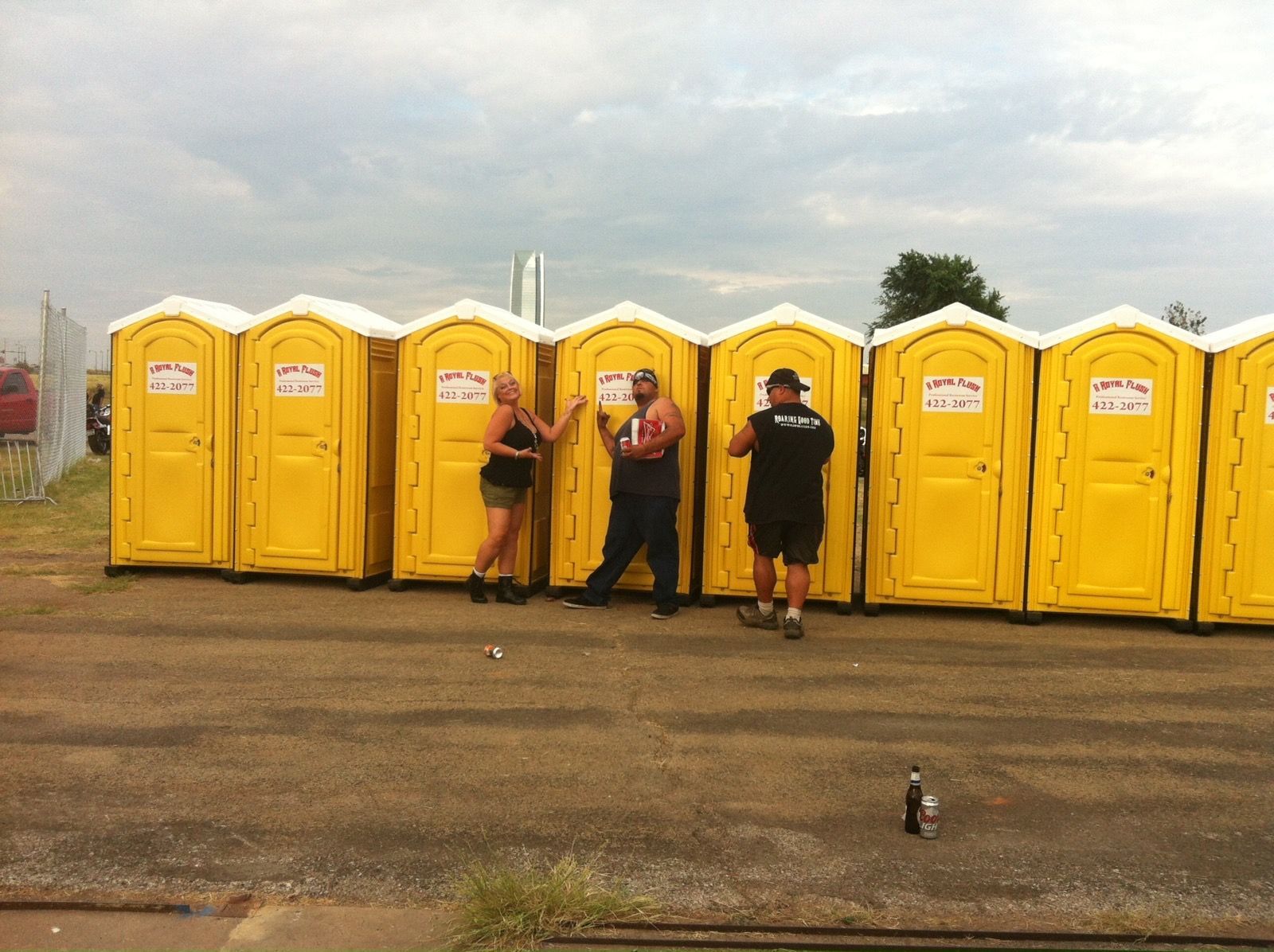 Three people pose in front of a row of yellow portable toilets.