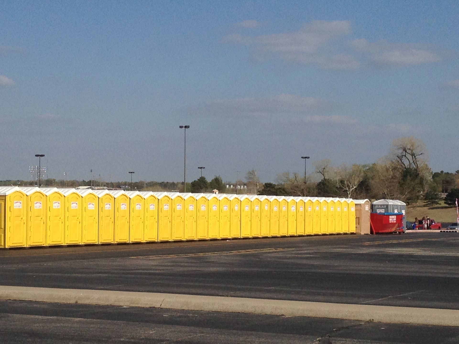 Yellow portable toilets in a row, with a red trailer, in a parking lot under a blue sky.