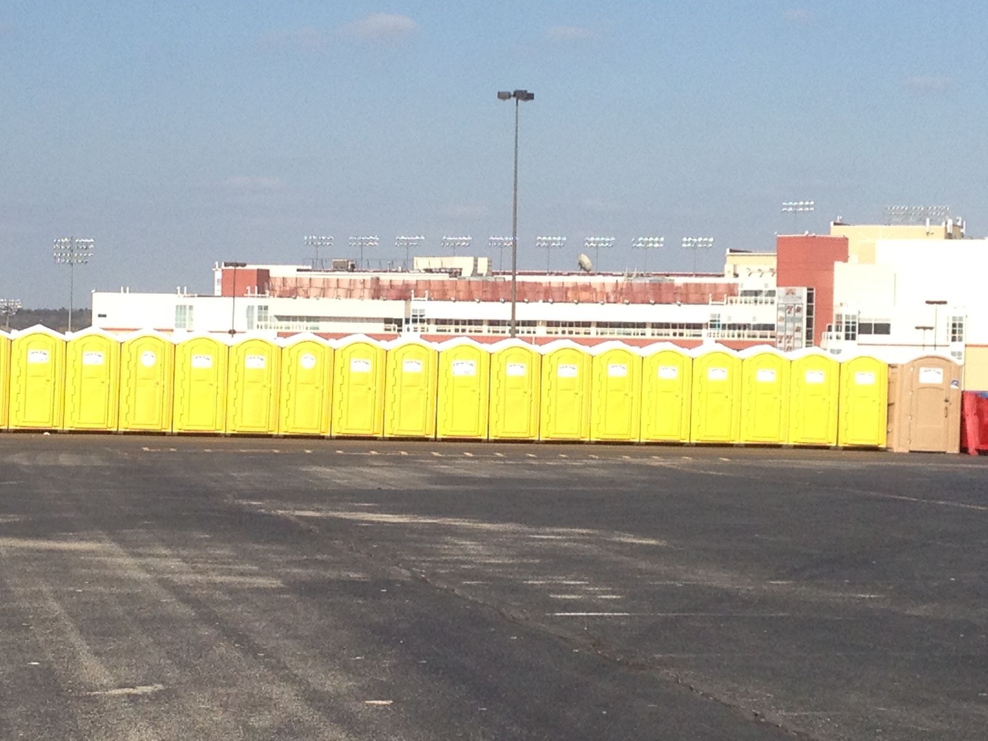 Row of yellow portable toilets in a parking lot, with a building in the background.