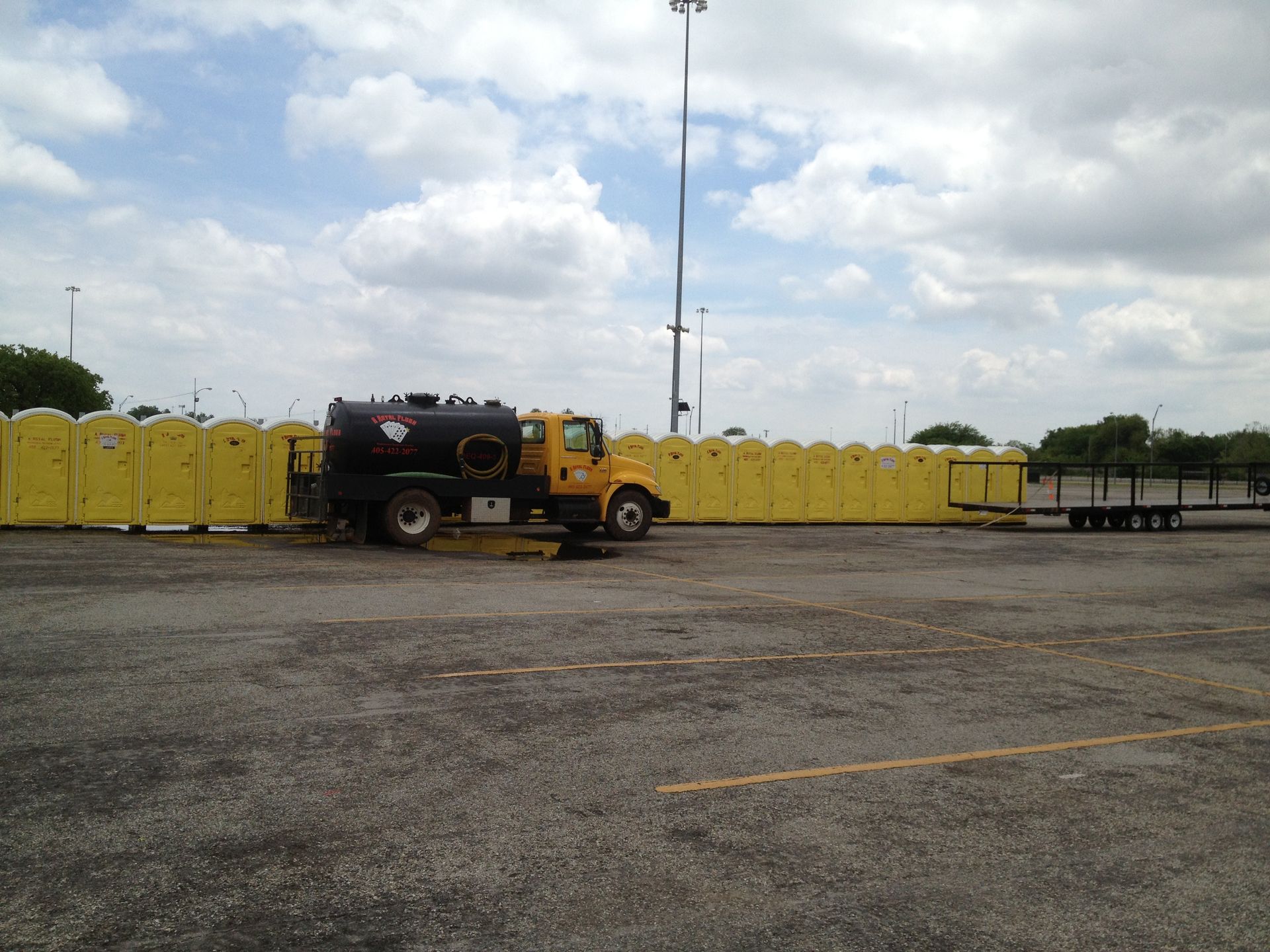 Yellow truck parked in a parking lot, servicing a long row of yellow portable toilets.