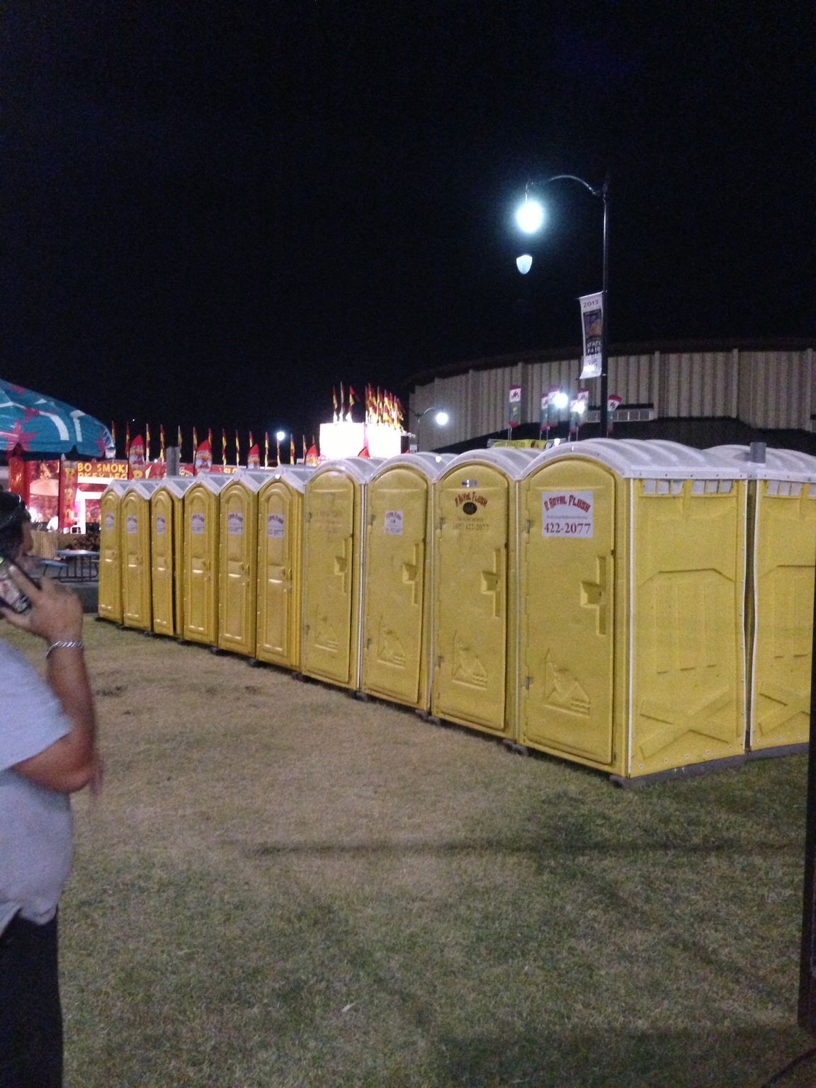 A row of yellow portable toilets at night, likely at an outdoor event.