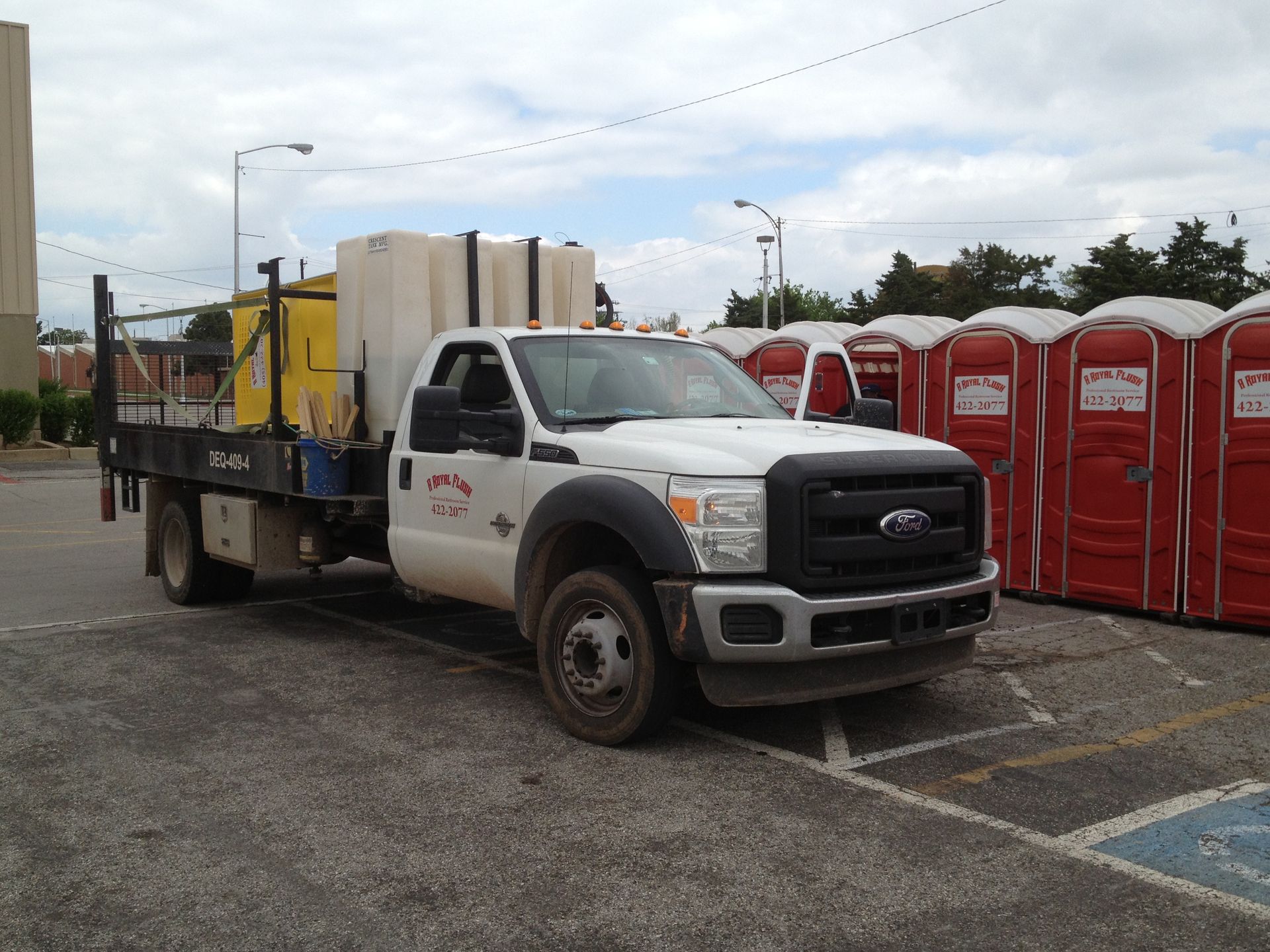White Ford flatbed truck with equipment beside a row of red portable toilets.