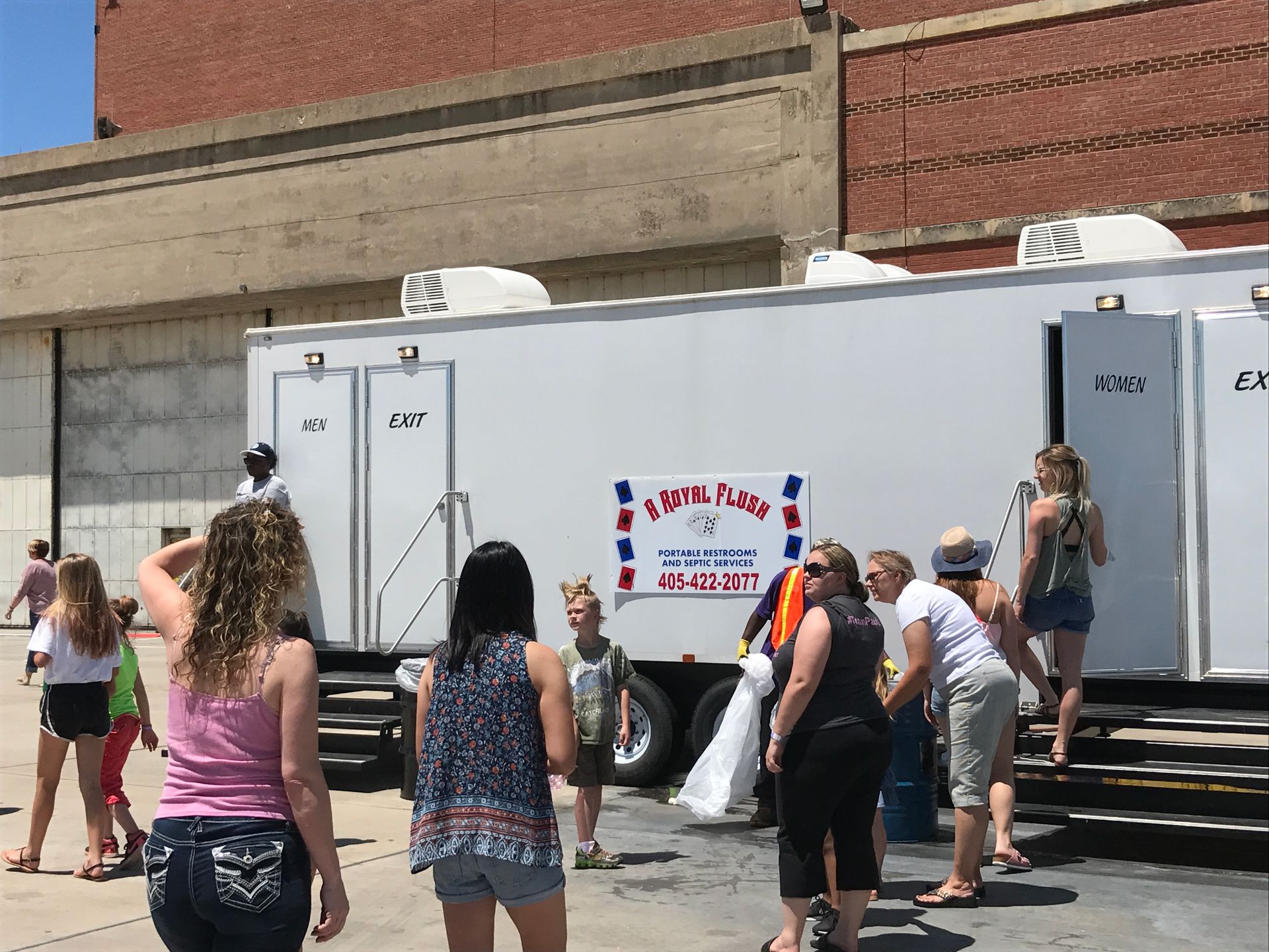 Portable restrooms with people waiting outdoors, brick building background.