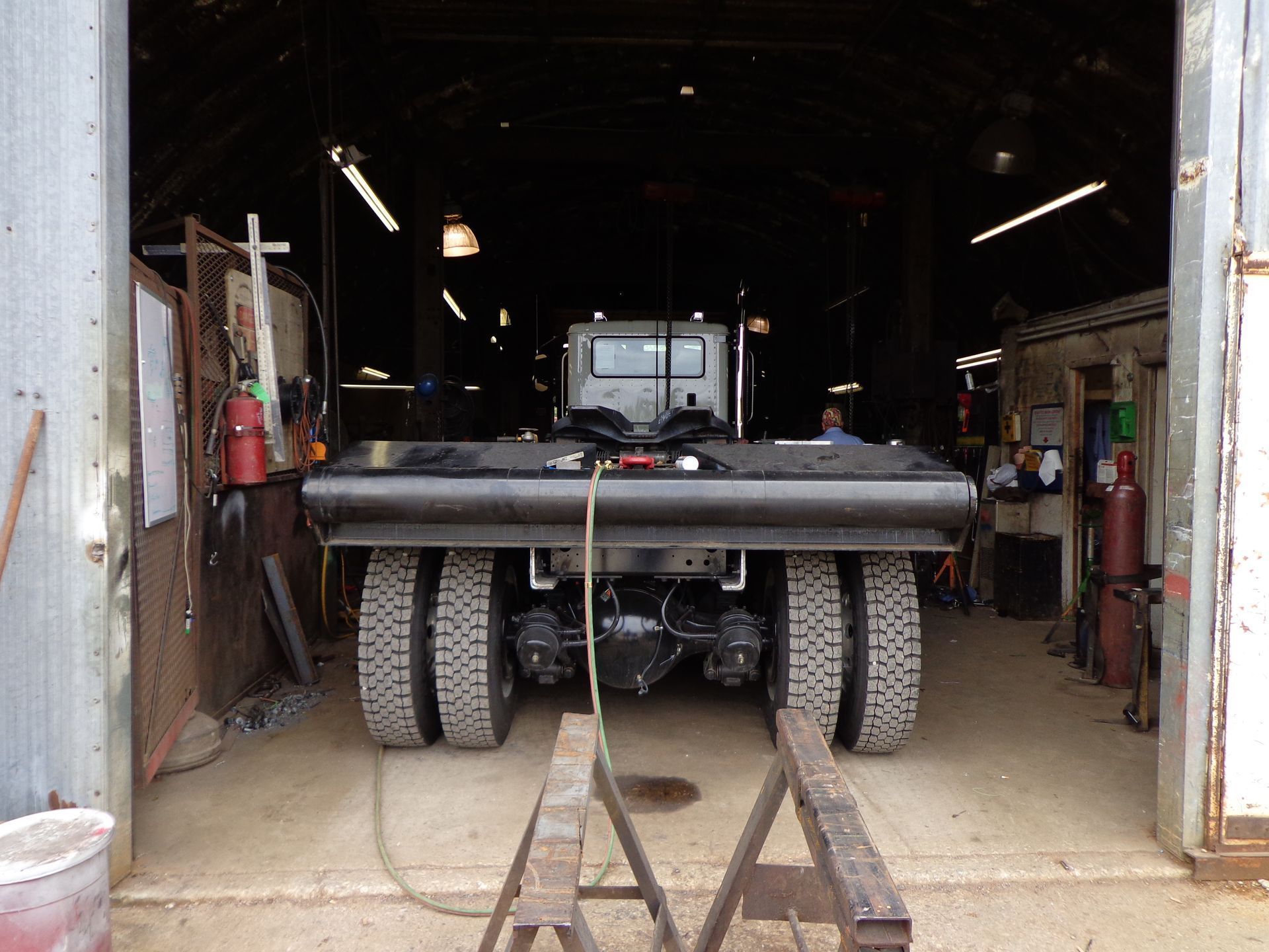 A heavy-duty truck, seen from behind, sits in a dark, open-bay industrial workshop.