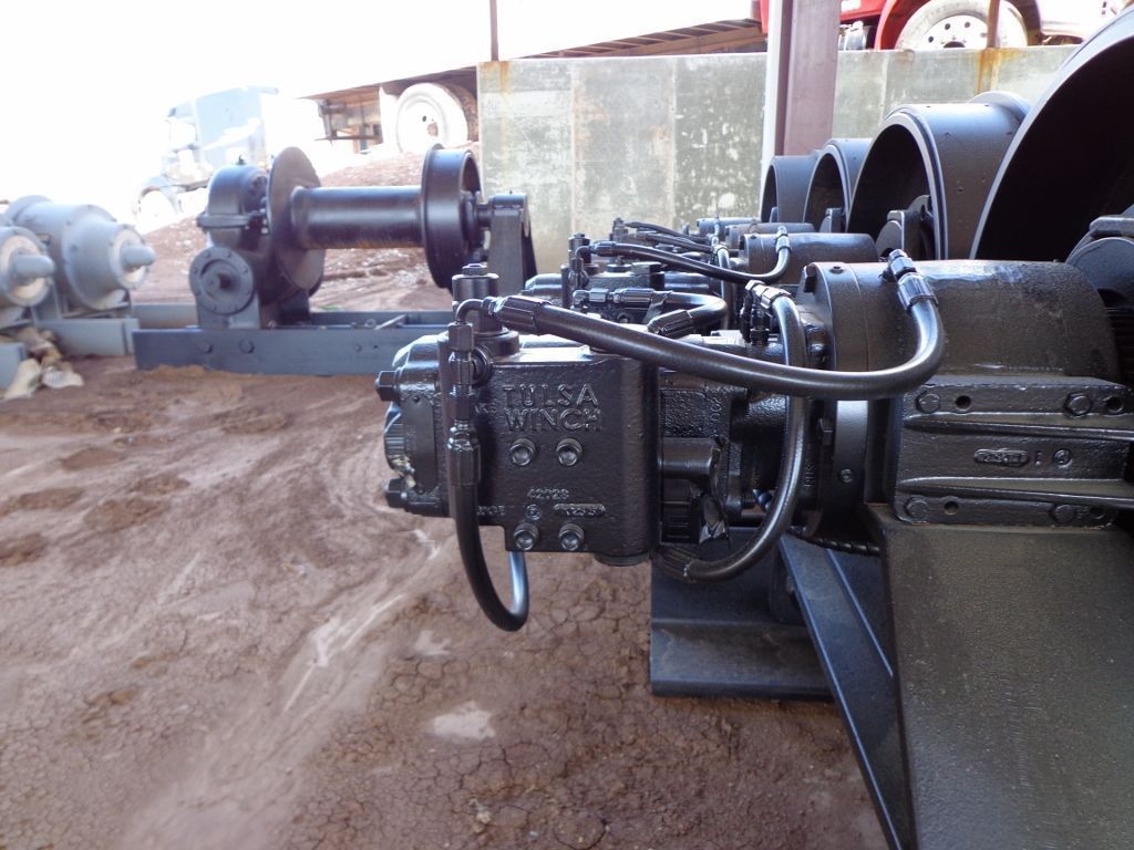 Industrial equipment with a black hydraulic motor and winch assembly sits on dirt, with spare parts in the background.