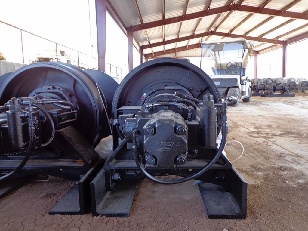 Two industrial winch units sit in a covered outdoor facility, with a vehicle visible in the background.