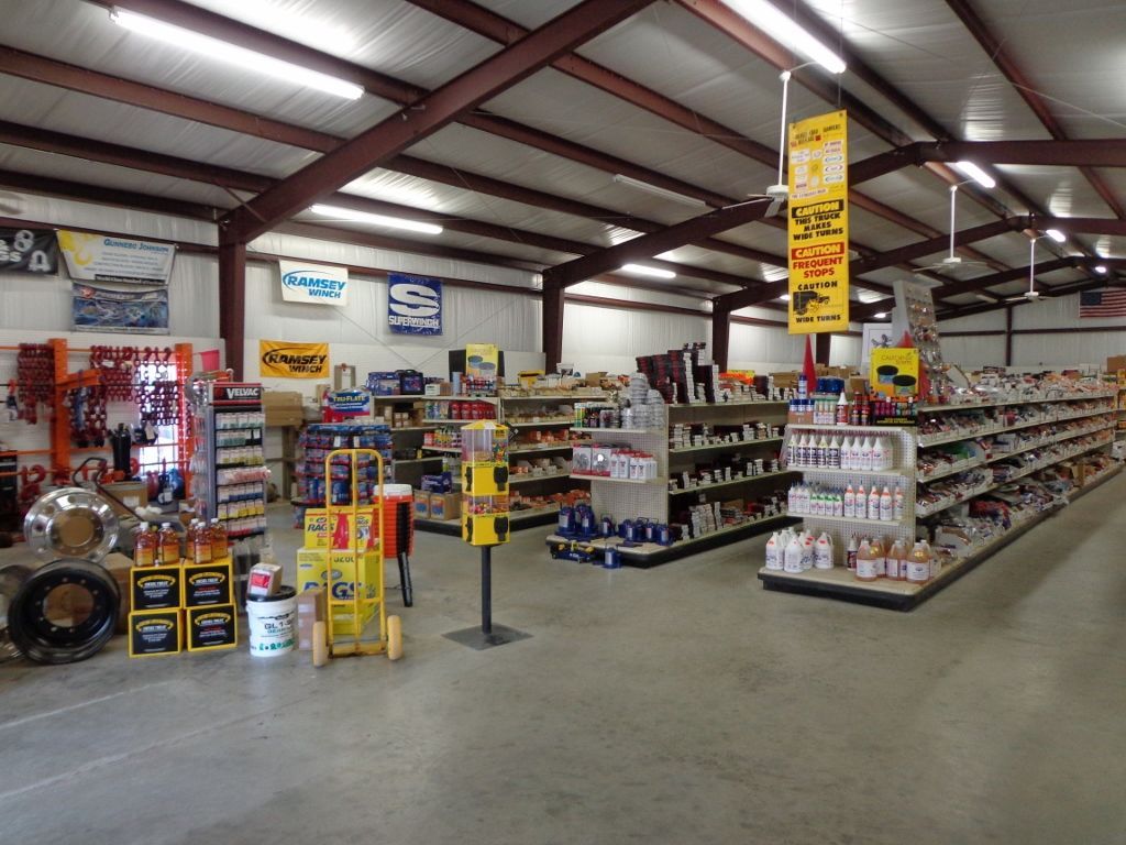 Warehouse store aisle with shelves of auto parts and tools under bright fluorescent lights