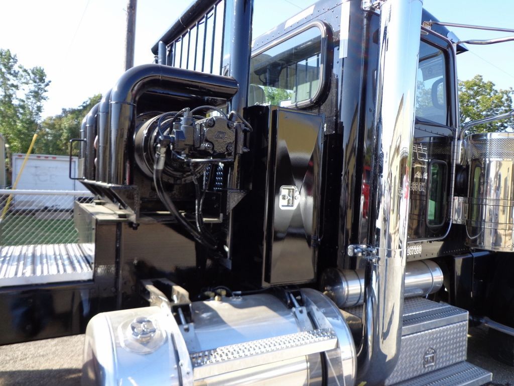 Close-up of a black semi-truck cab with chrome exhaust pipes, side steps, and a headache rack behind the driver door.