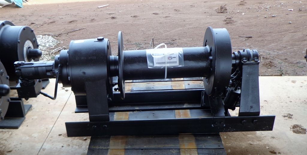A black industrial winch mounted on a metal frame, positioned outdoors on a concrete surface.