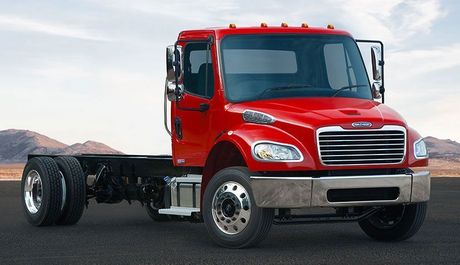 A bright red Freightliner medium-duty truck chassis cab parked against a desert horizon.
