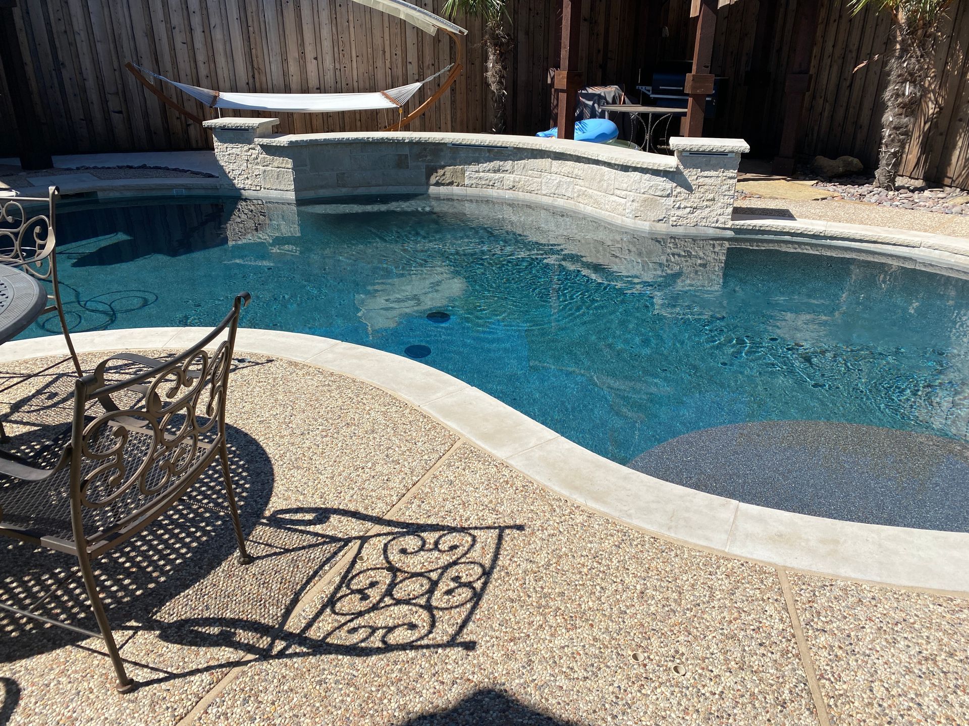 A large swimming pool with a table and chairs in front of it.