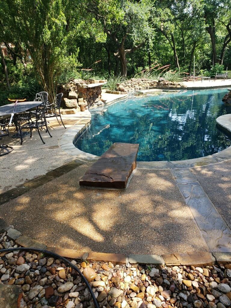A large swimming pool surrounded by rocks and trees in a backyard.