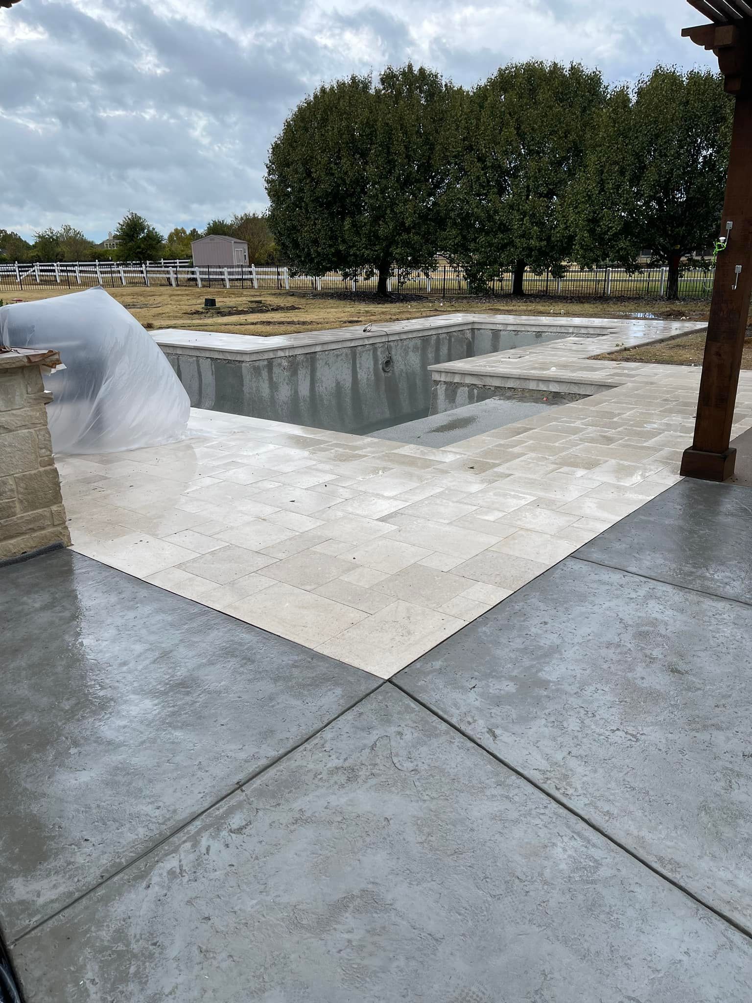 A concrete patio with a swimming pool in the background.