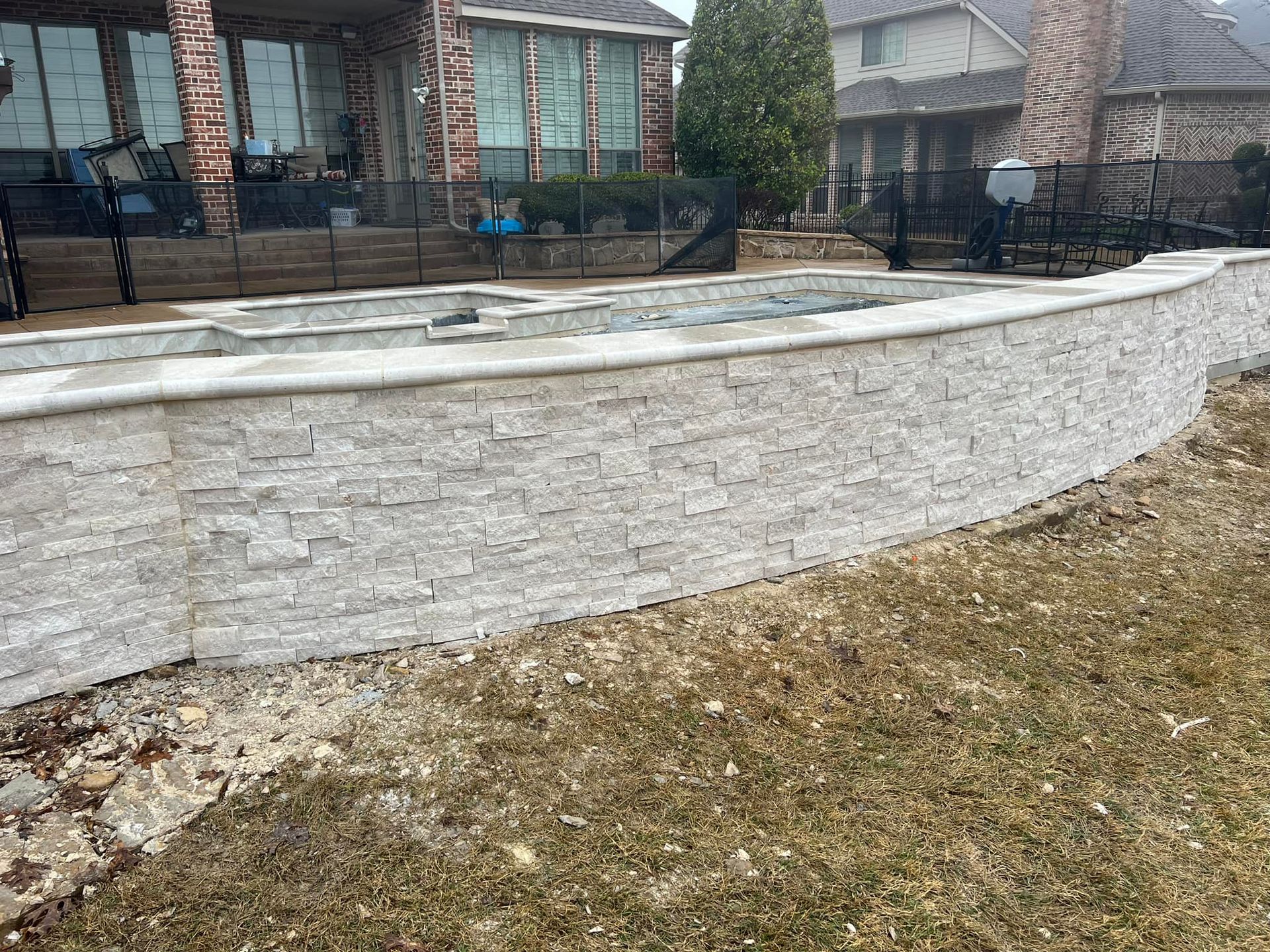 A large brick wall is surrounding a pool in a backyard.