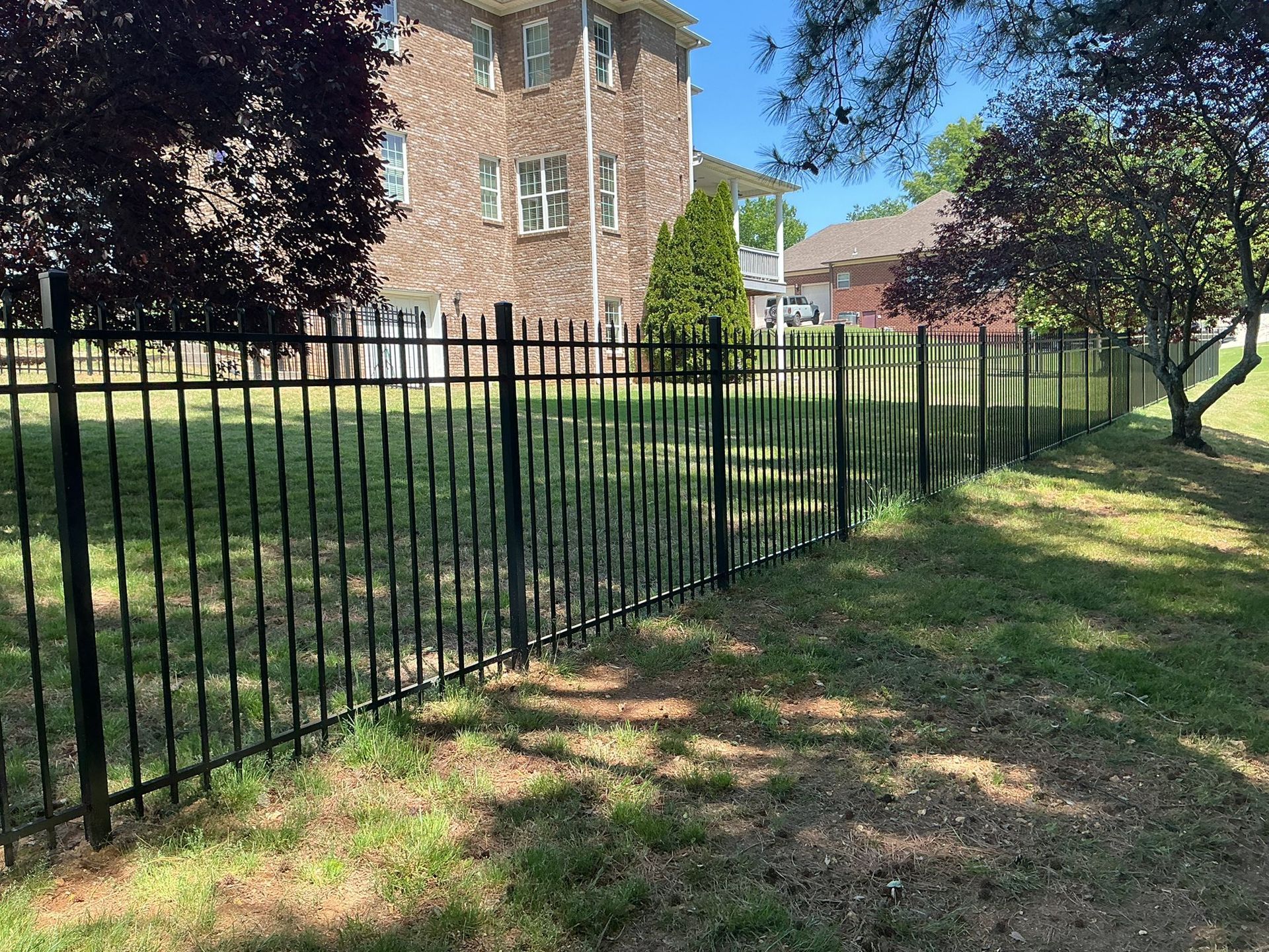 Black metal fence beside a grassy yard and brick apartment building on a sunny day