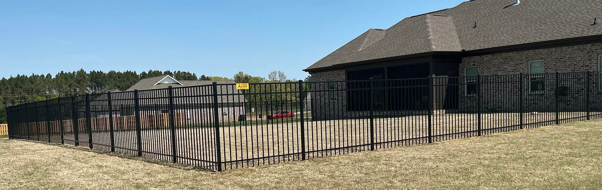 Fenced yard beside a dark wooden house with a covered porch in a sunny, dry landscape