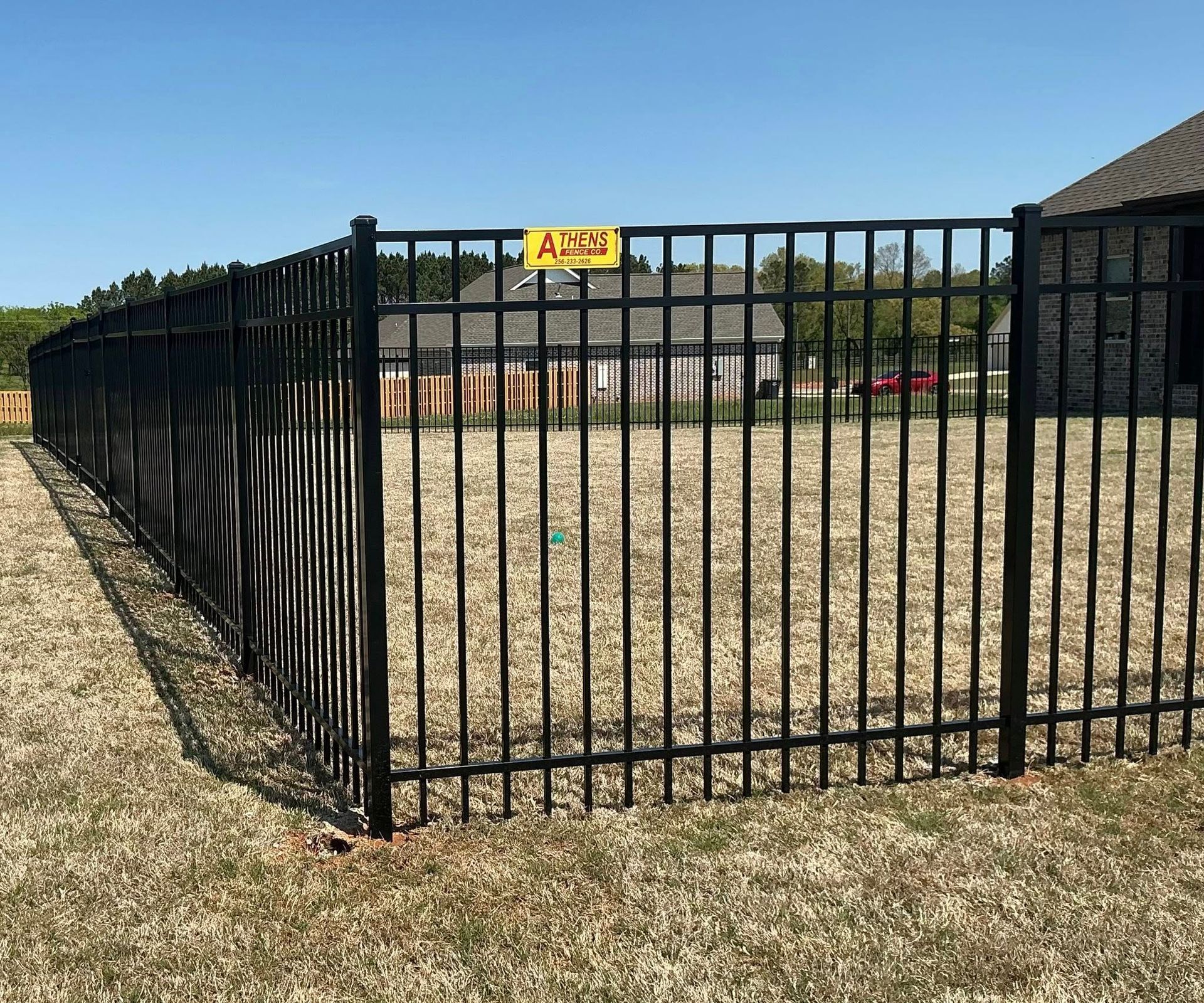 Black metal fence around a gravel yard with a yellow sign, under a clear blue sky.