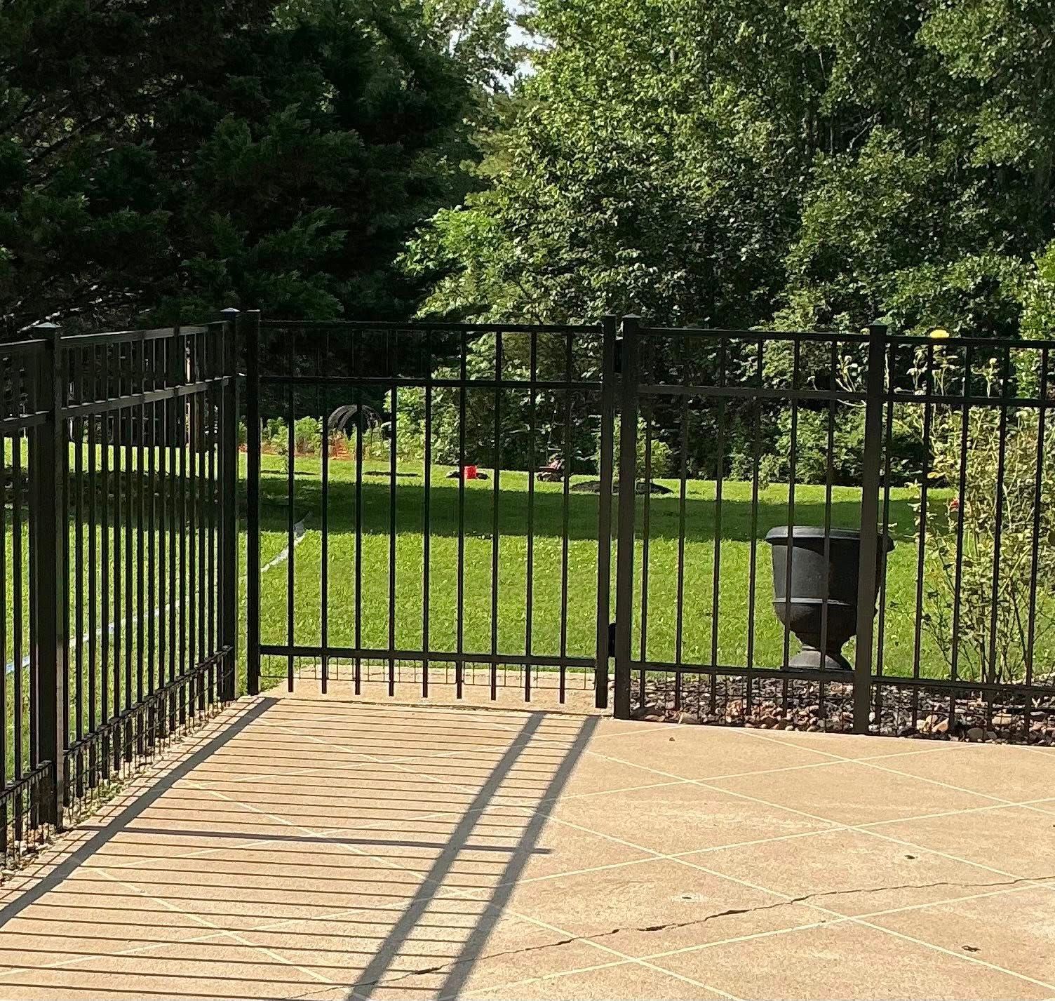 Black metal fence around a sunlit patio beside a green park and trees