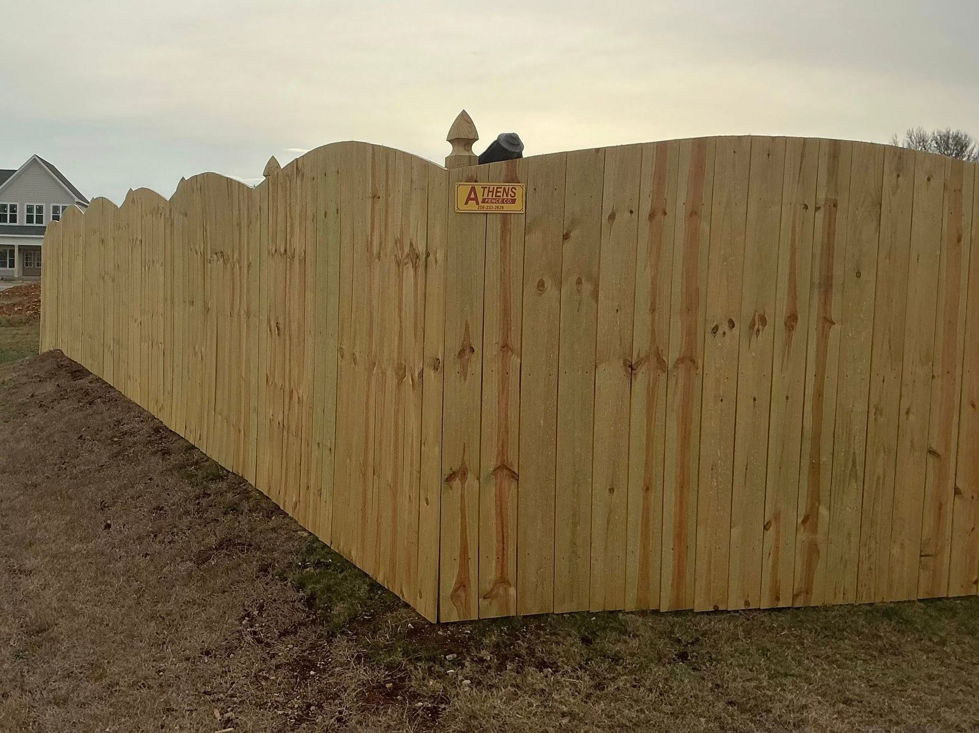 Wooden privacy fence with a rounded corner in a grassy yard under a cloudy sky