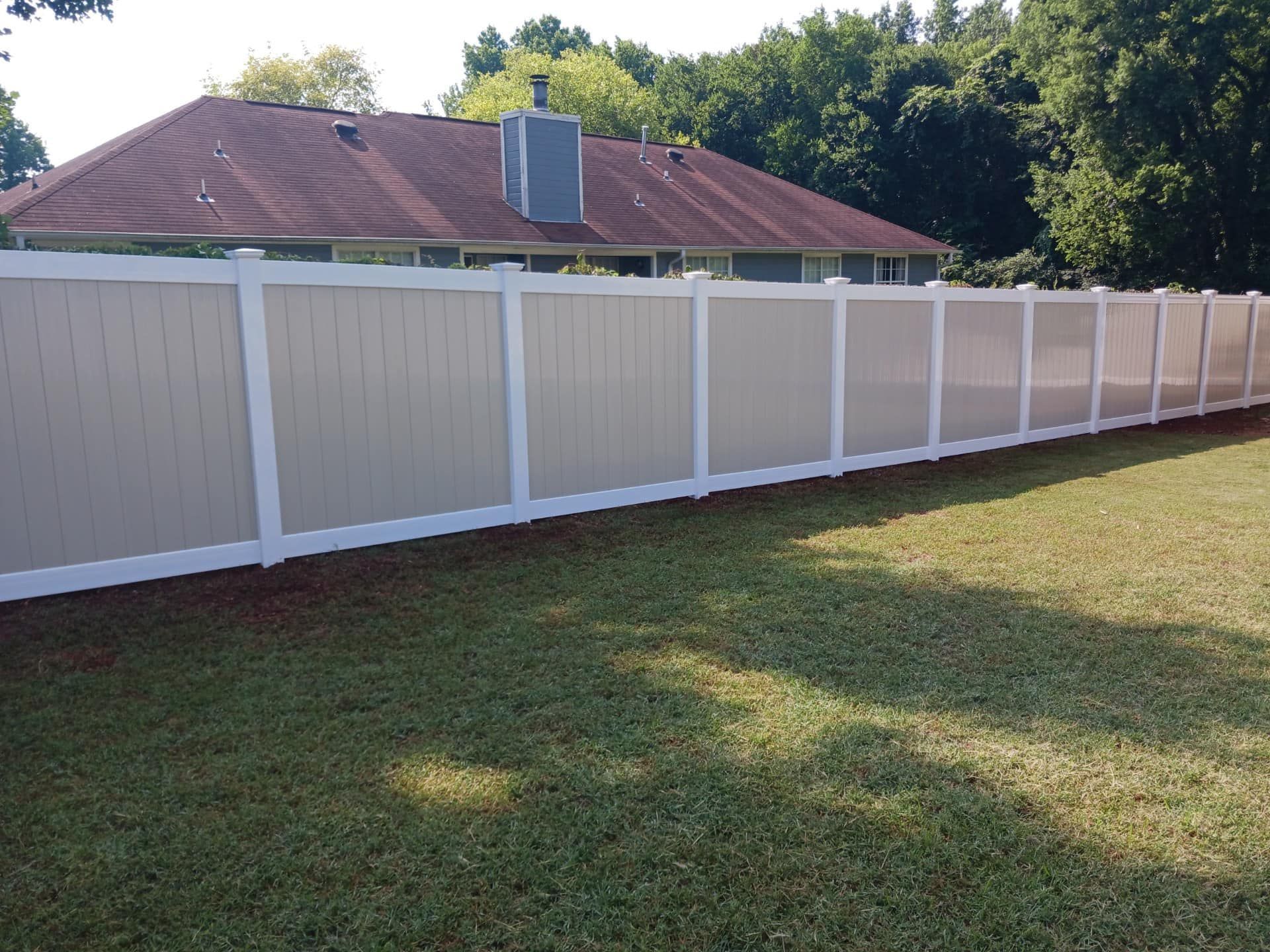 Long white privacy fence along a grassy yard beside a red-roofed house.