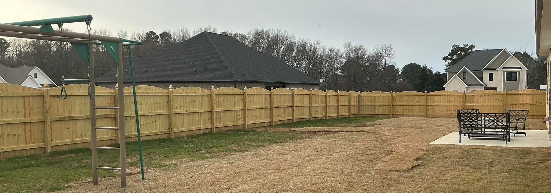 Wooden fence around a gravel yard with a slide on the left and picnic table on the right under a cloudy sky