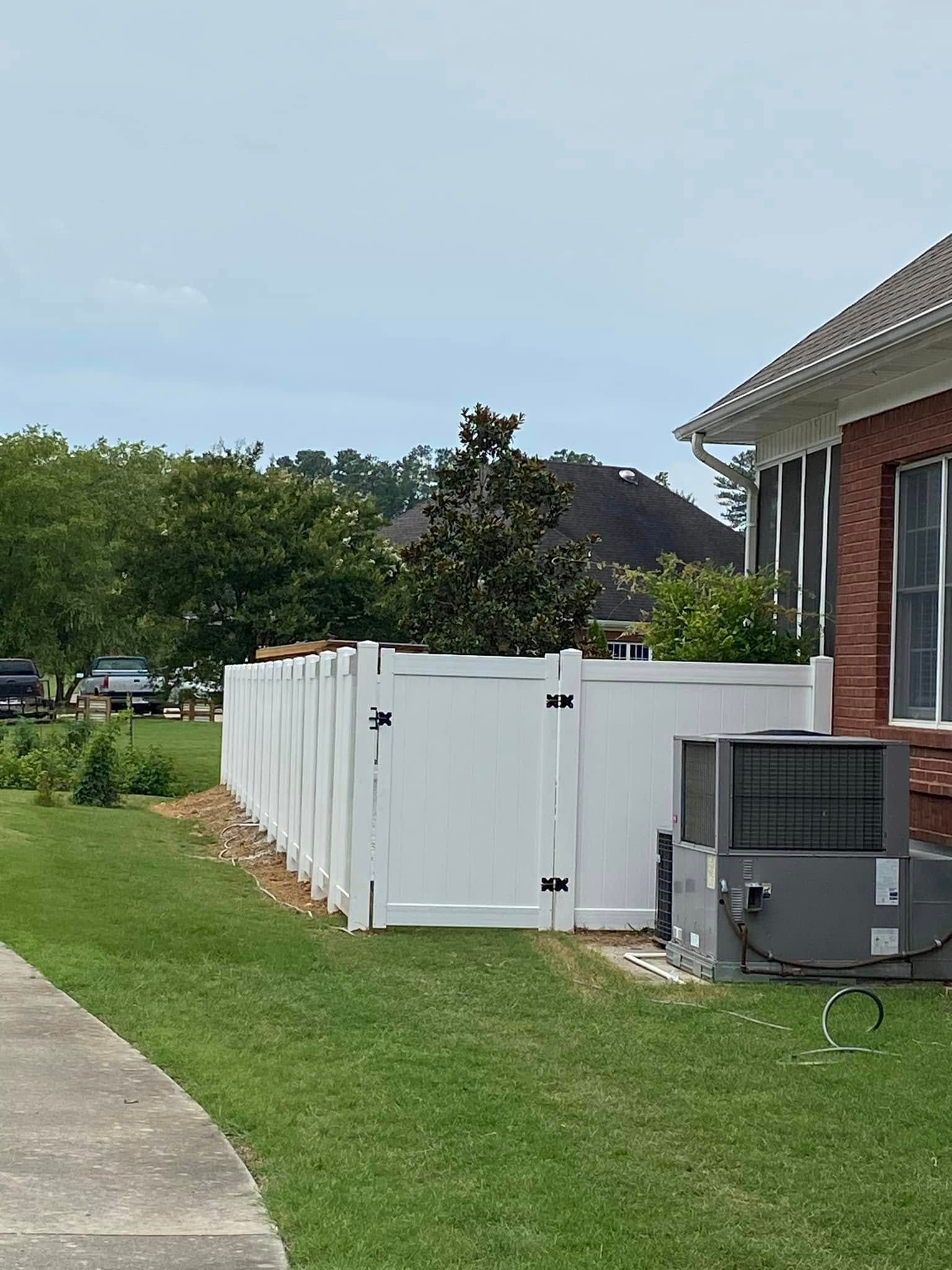 White fence panels beside a brick house, with an air conditioner unit on a grassy lawn.