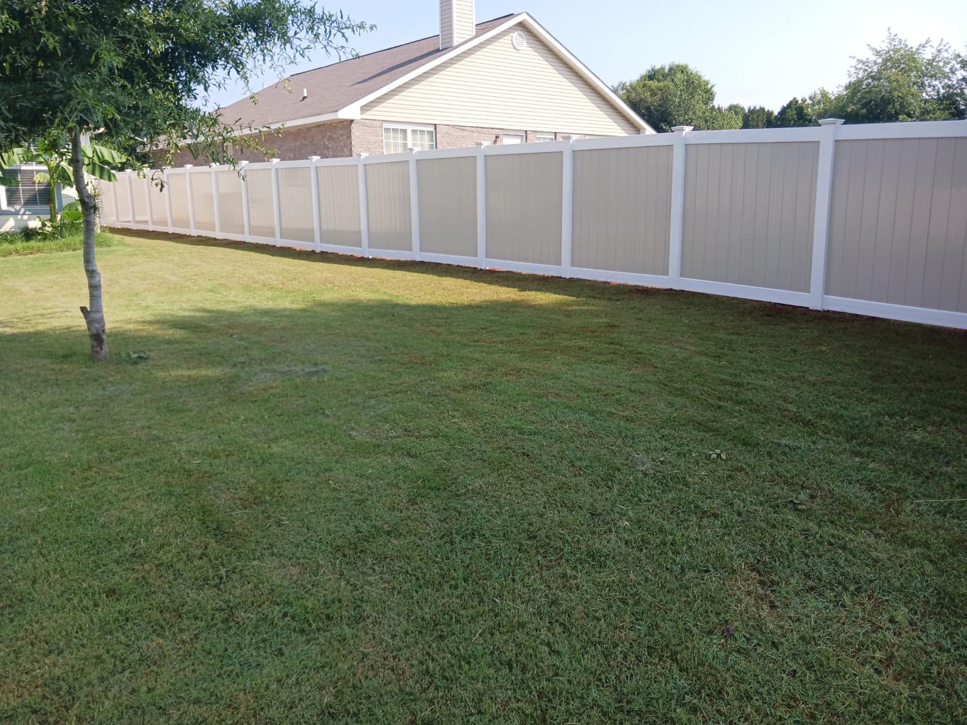 Backyard lawn with a white vinyl fence and a house in the background