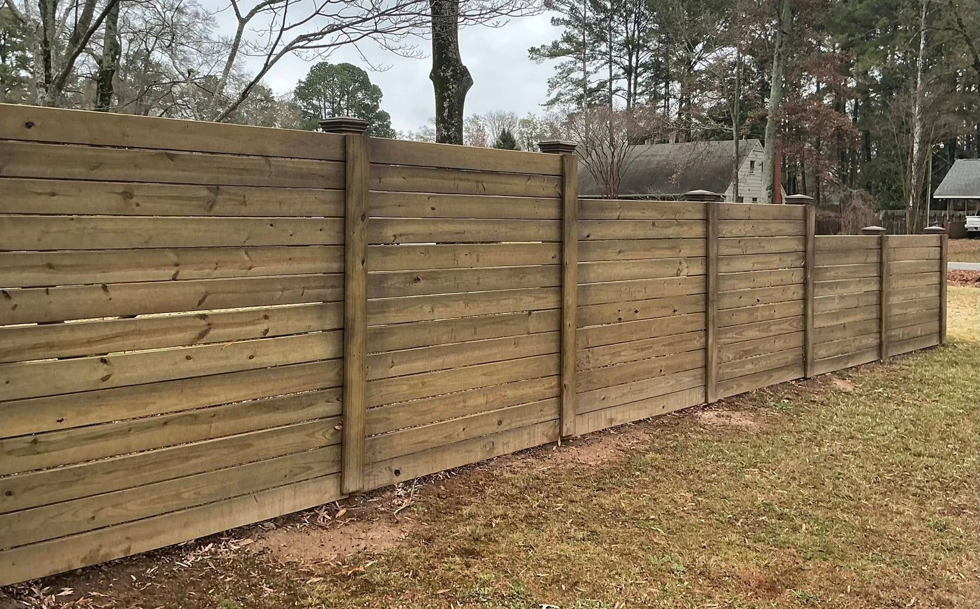 Long wooden privacy fence along a grassy yard with trees in the background