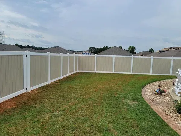 Backyard with green lawn, white vinyl fence, and curved rock landscaping under a cloudy sky