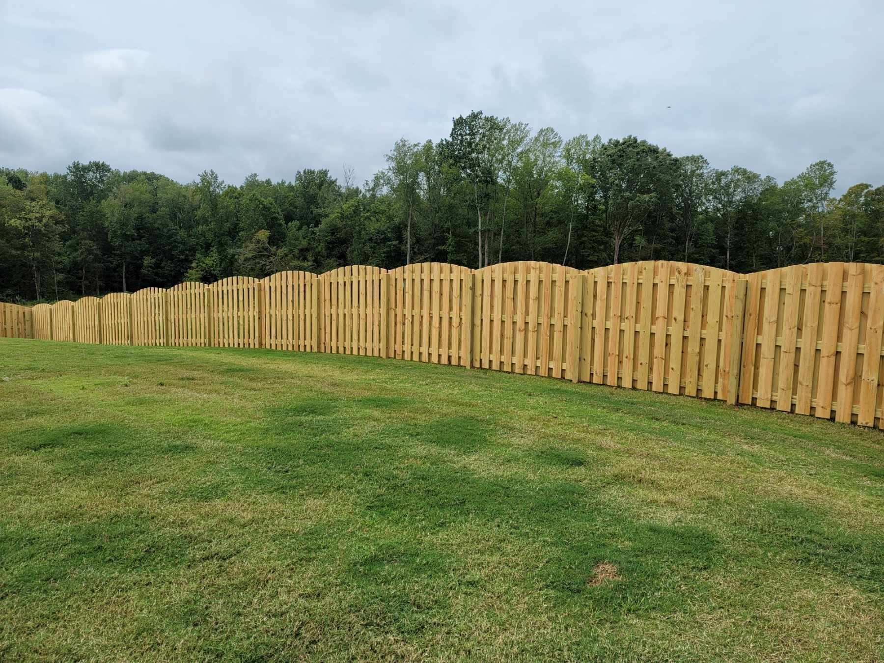 Curved wooden fence along a grassy field with trees and cloudy sky in the background