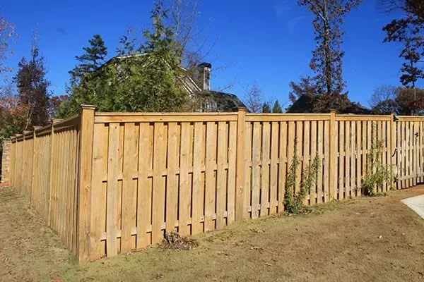 Wooden privacy fence with gate in a grassy yard under a clear blue sky