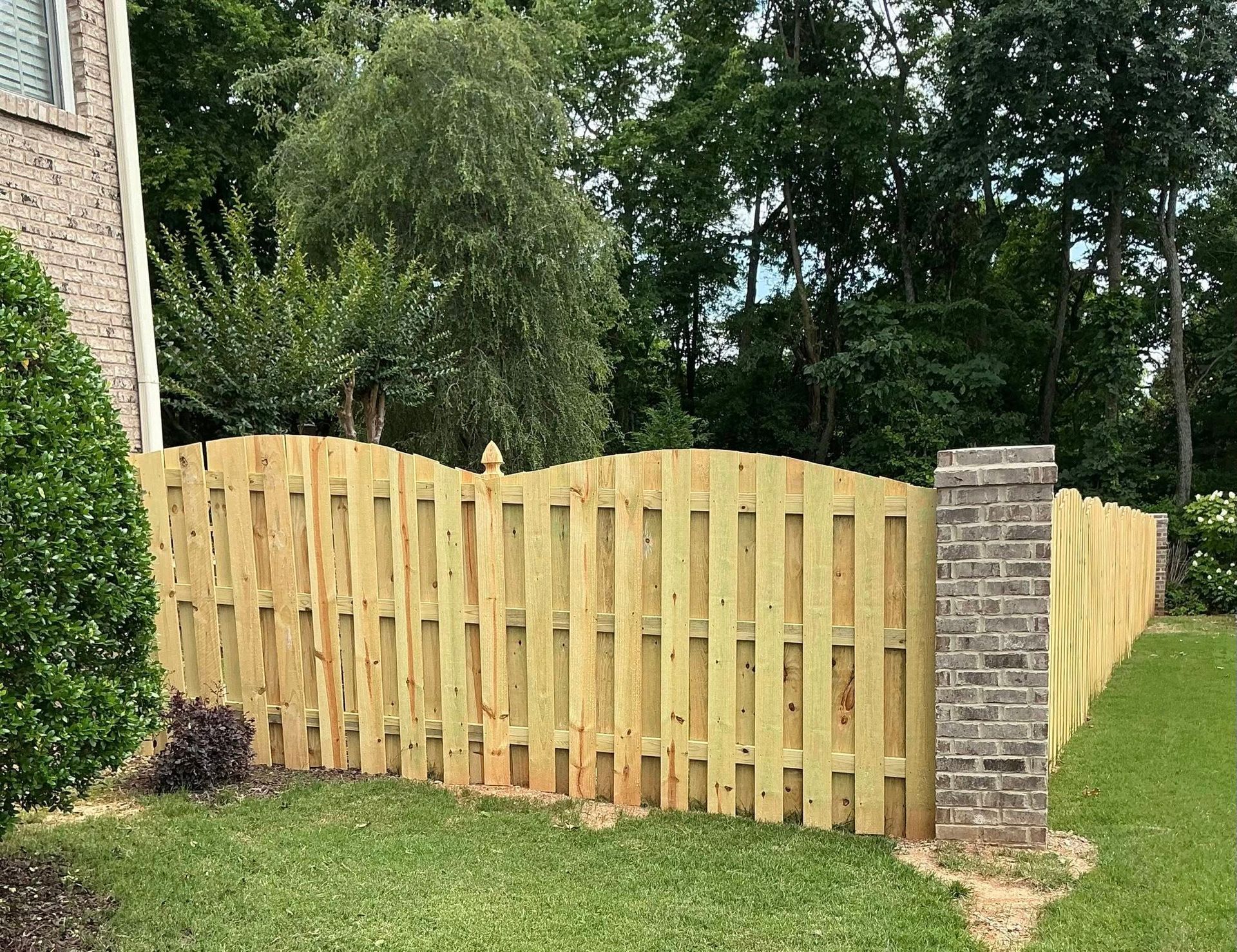 Light wooden fence with brick pillars along a green yard beside a house and trees
