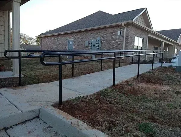 Accessible sidewalk ramp with handrails leading to a brick building entrance