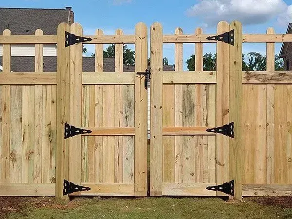 Wooden double gate with black hinges in a fenced yard under a blue sky