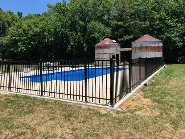 Fenced backyard with a small blue pool and two cylindrical tanks near trees.