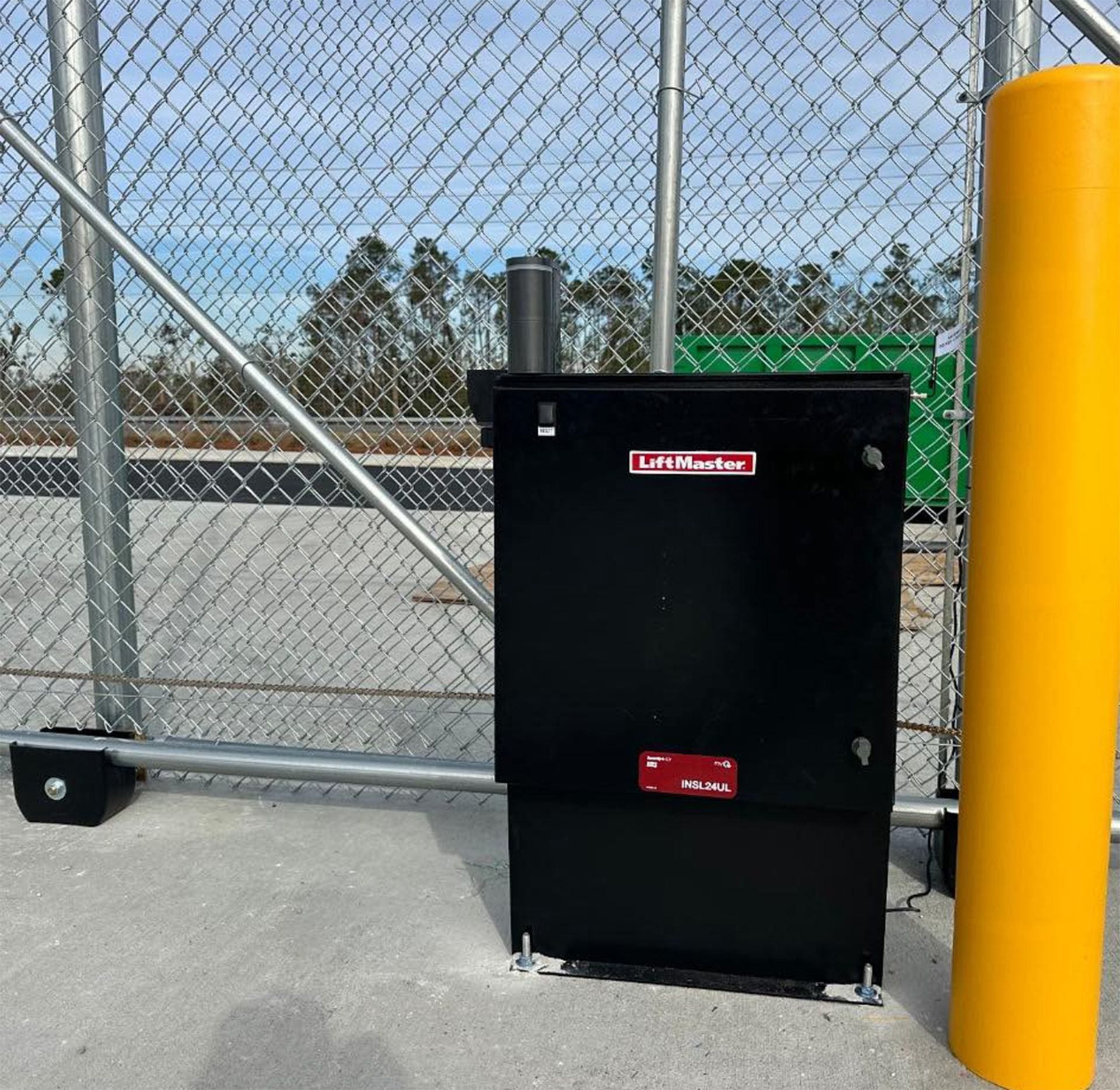 Hands wiring a small electronic device on a metal box beside a blue gate outdoors