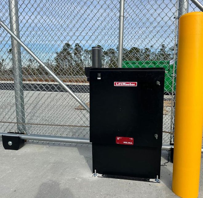Hands wiring a small electronic device on a metal box beside a blue gate outdoors