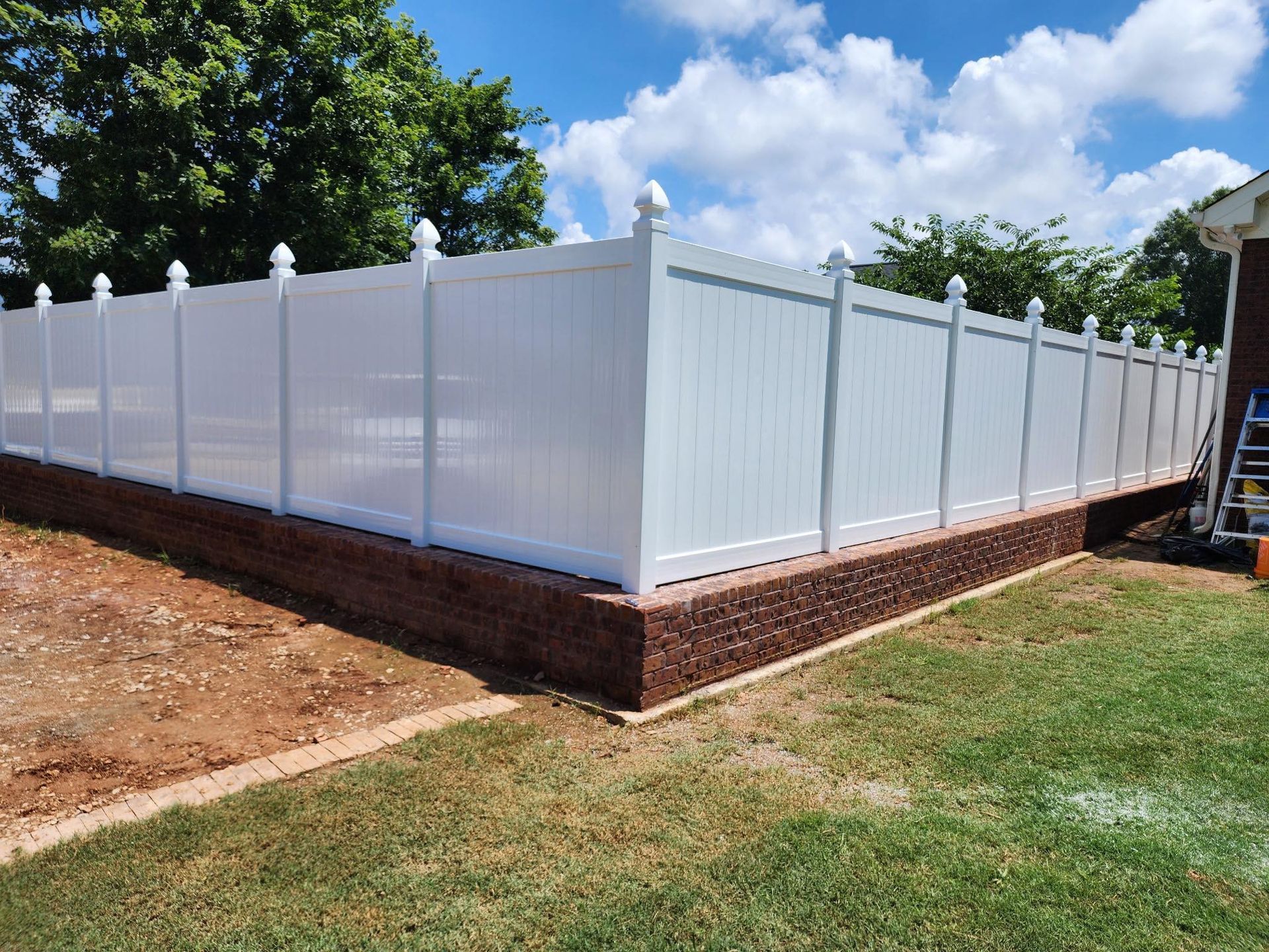 White vinyl privacy fence with brick base along a yard under a blue sky