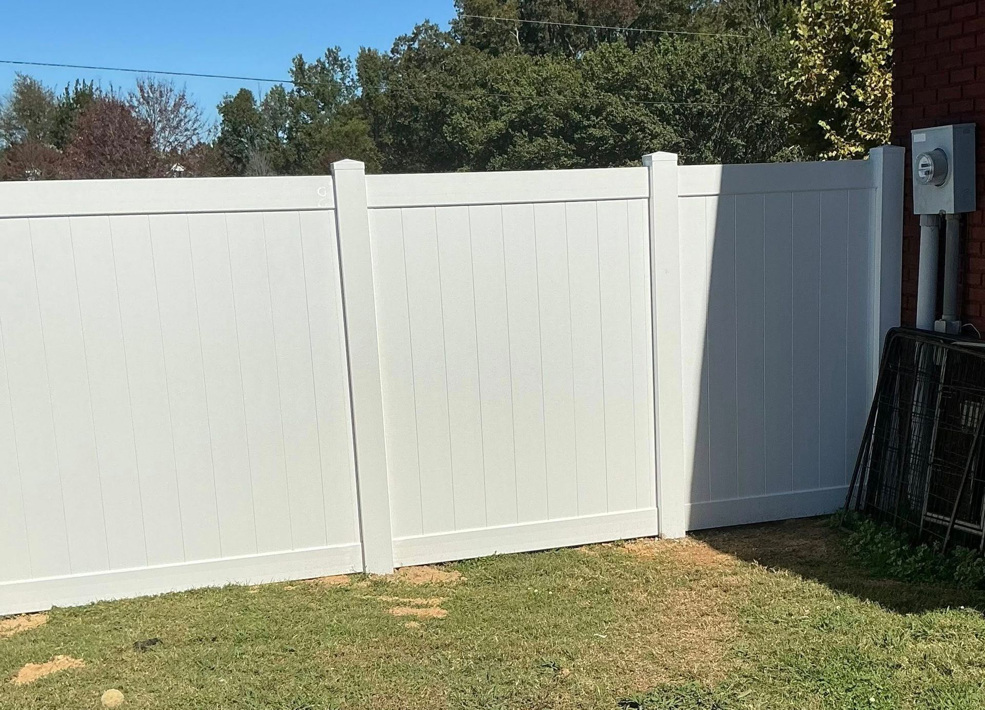 White vinyl fence with a gate in a sunny backyard under a blue sky