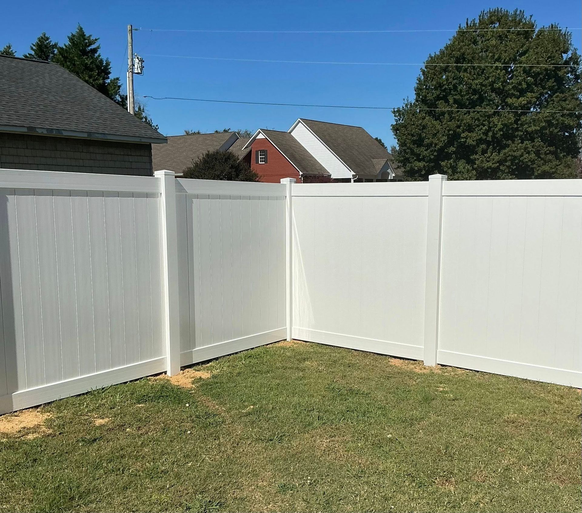 White vinyl privacy fence forming a corner in a sunny backyard with grass and neighboring houses beyond