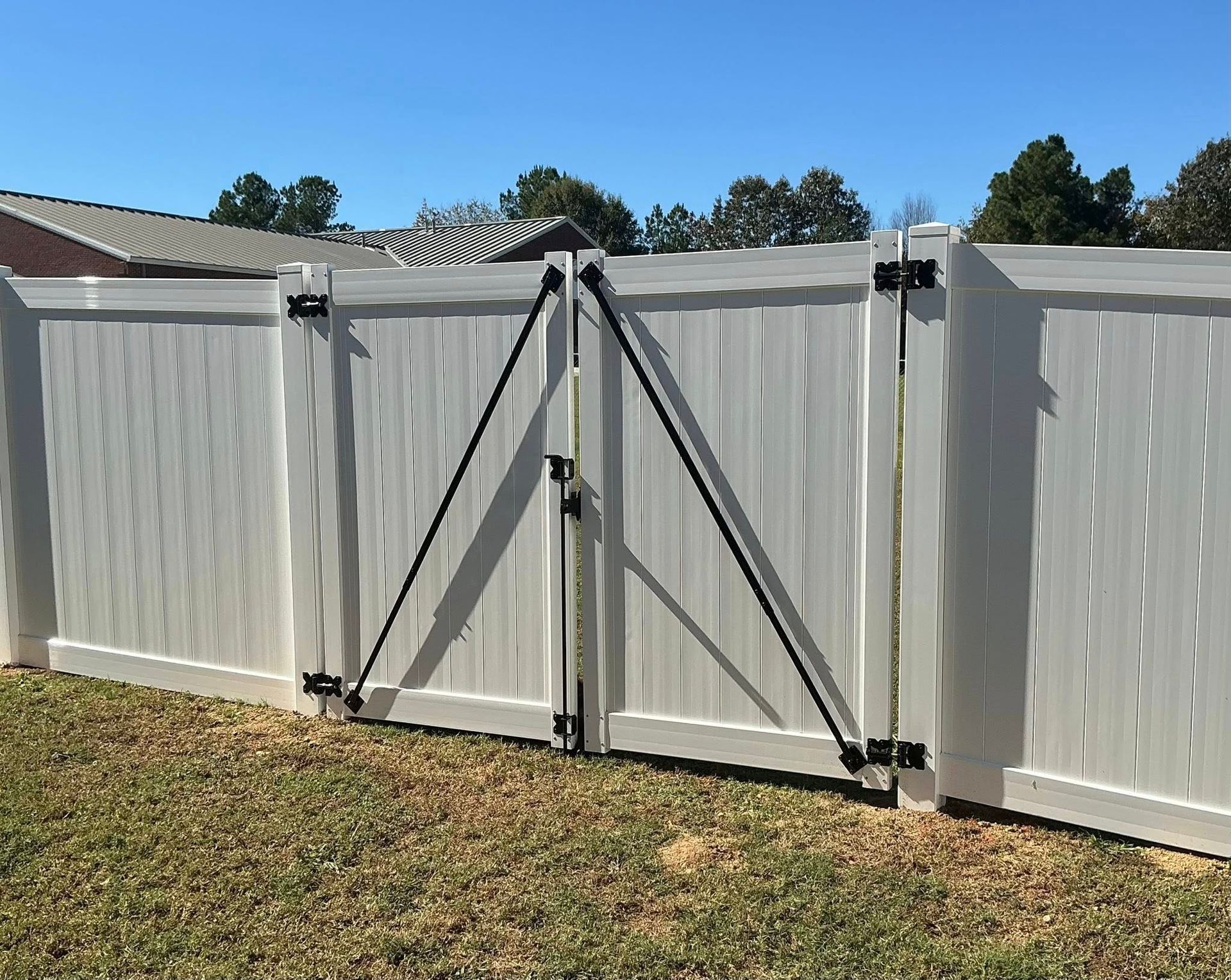 White vinyl backyard fence with a gray gate and diagonal support braces under a blue sky