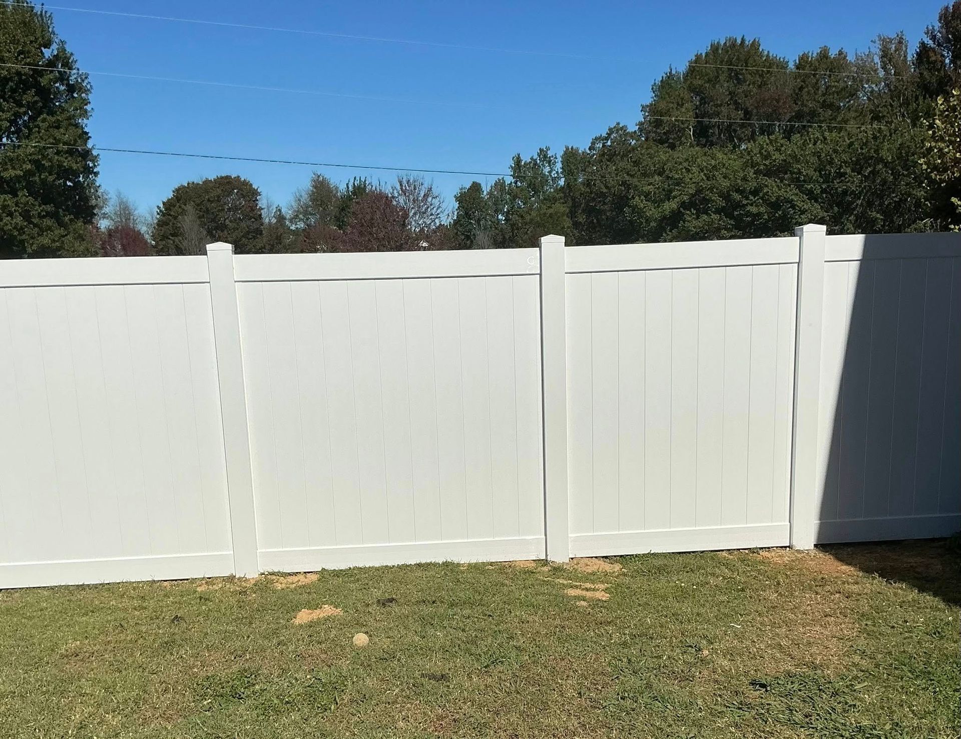 White vinyl fence along a grassy yard under a clear blue sky.