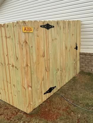 Wooden storage shed with black hinges and latch, beside a house on a grassy yard.