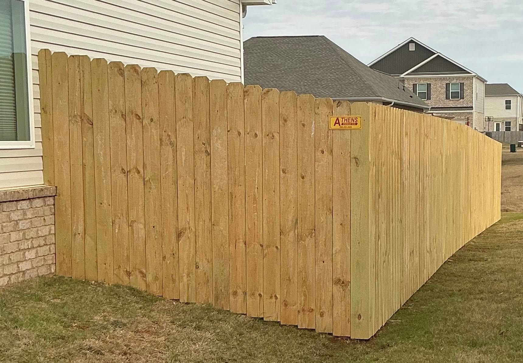 Wooden privacy fence enclosing a side yard beside a house, with neighboring homes in the background