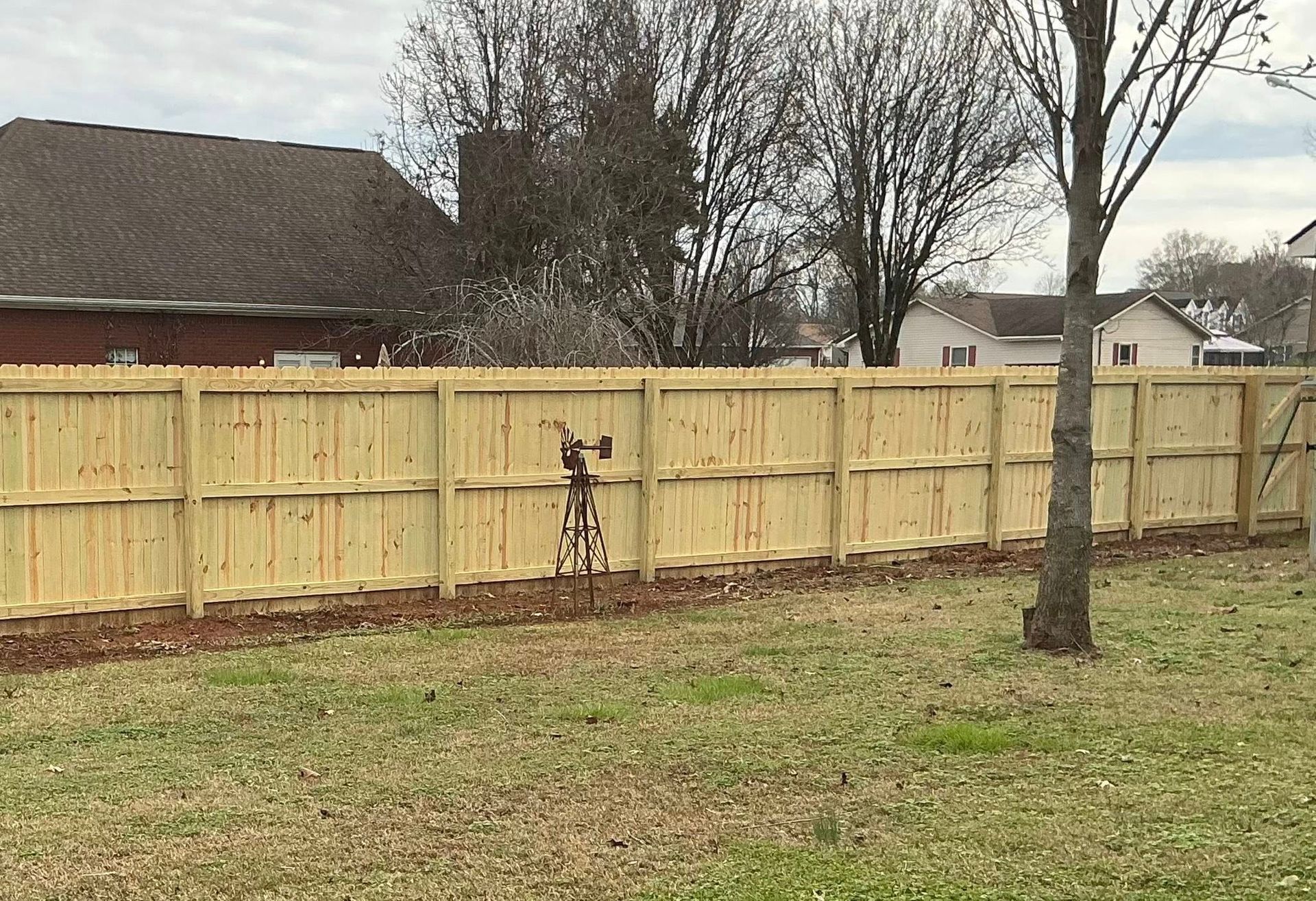 Backyard with a wooden fence, leafless trees, and a small metal sculpture near the center.