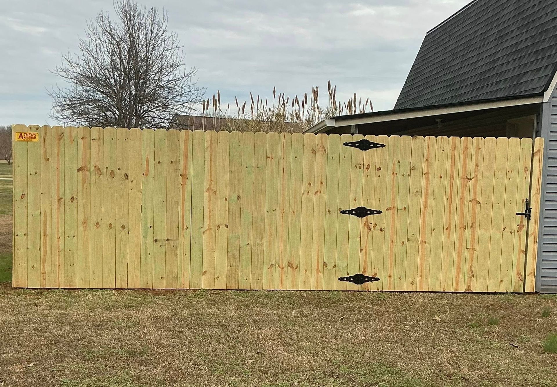 Wooden privacy fence with black hinges beside a house in a grassy yard