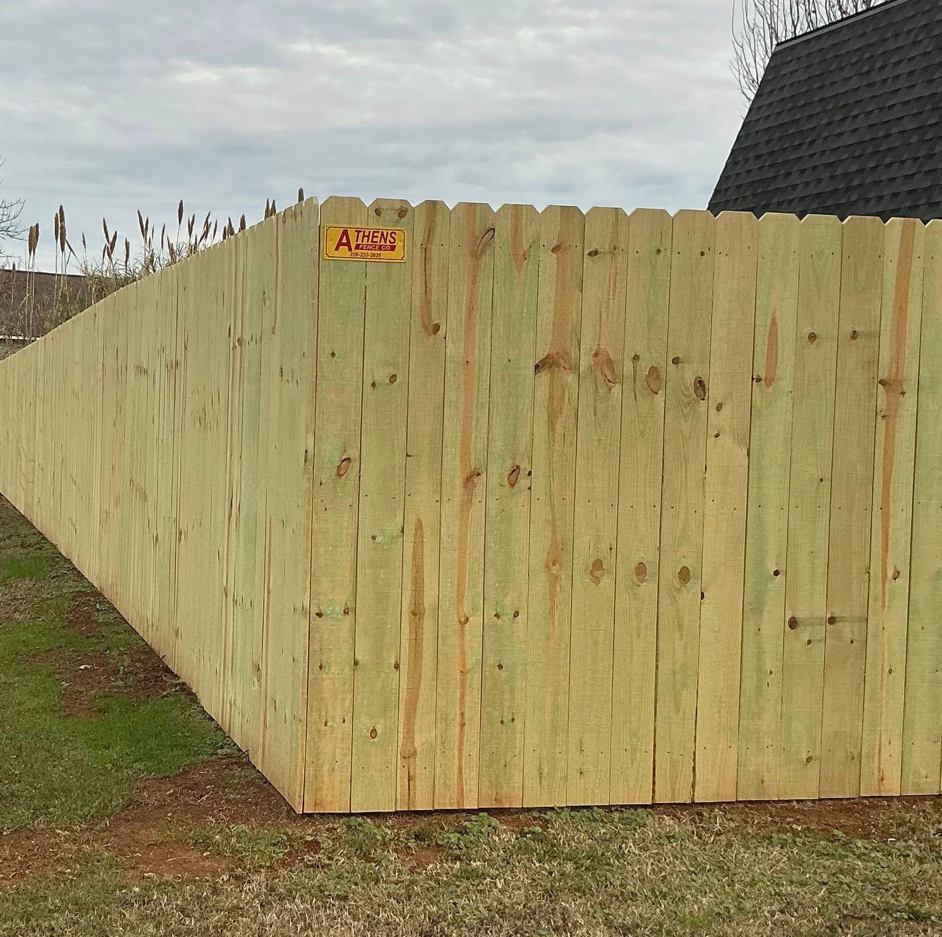 Tall unfinished wooden fence beside a house, with a small warning sign near the top.