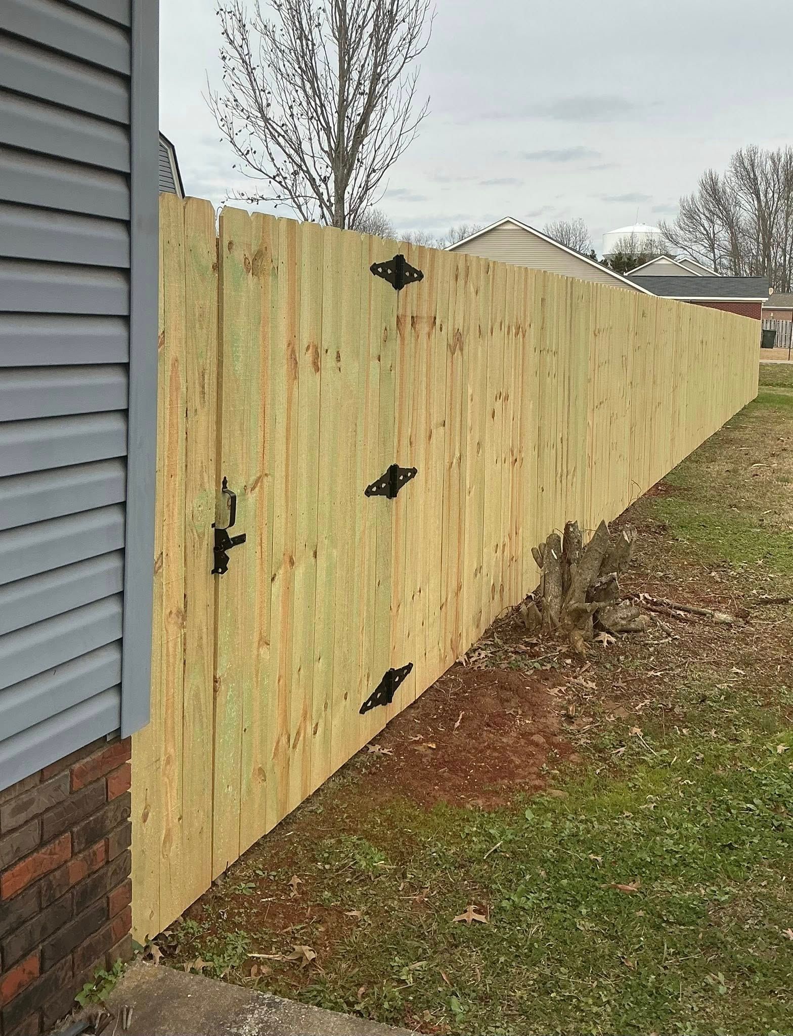 Wooden gate with black hinges beside a gray house and brick wall in a yard
